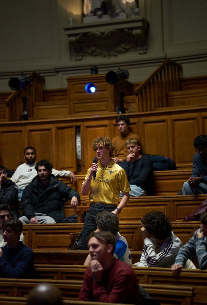 Un &eacute;tudiant pose sa question debout dans les gradins